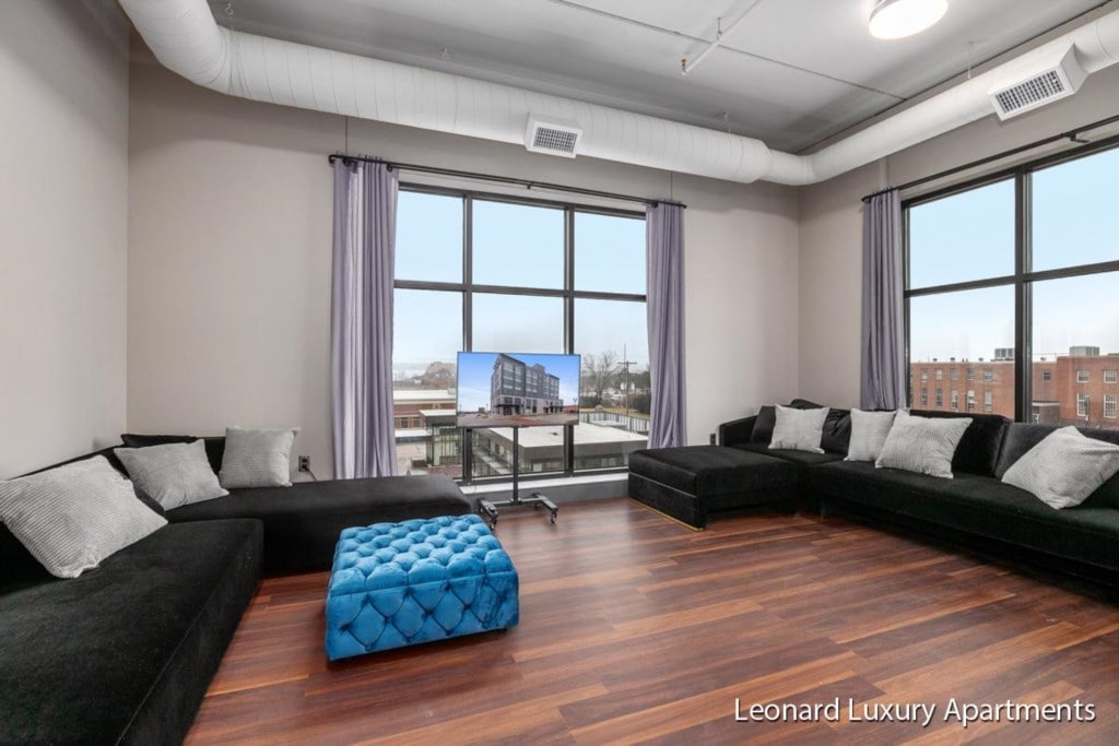Living room with large windows and blue ottoman at Downtown Muskegon Apartment #306