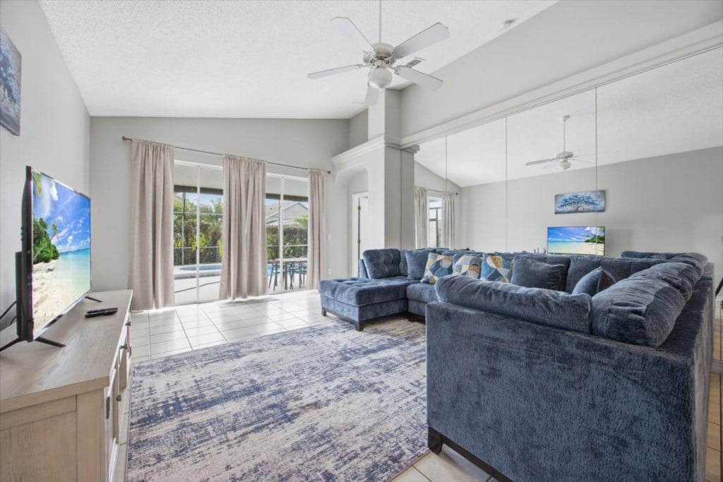 Bright living room with blue sofas and sliding doors opening toward the pool
