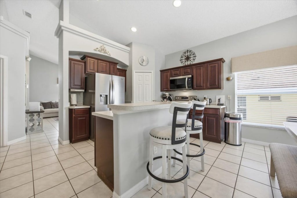 Open kitchen with dark wood cabinets, breakfast bar, and three stools