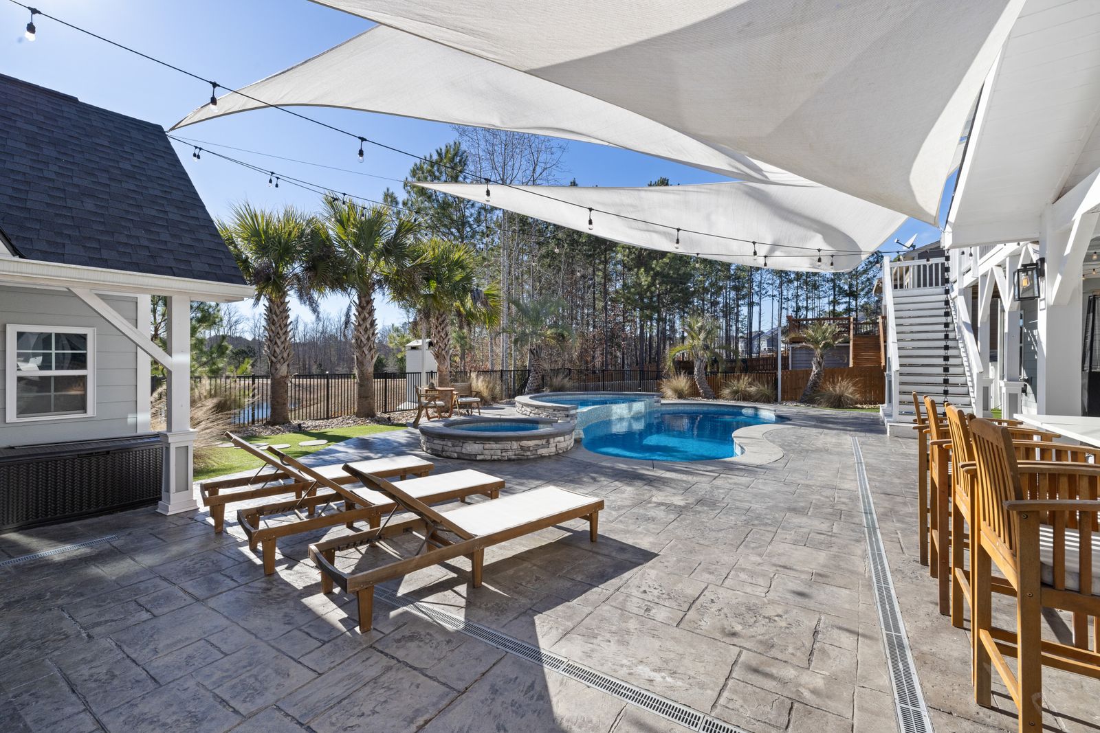 Backyard pool with lounge chairs, palms and sun sails under a clear sky