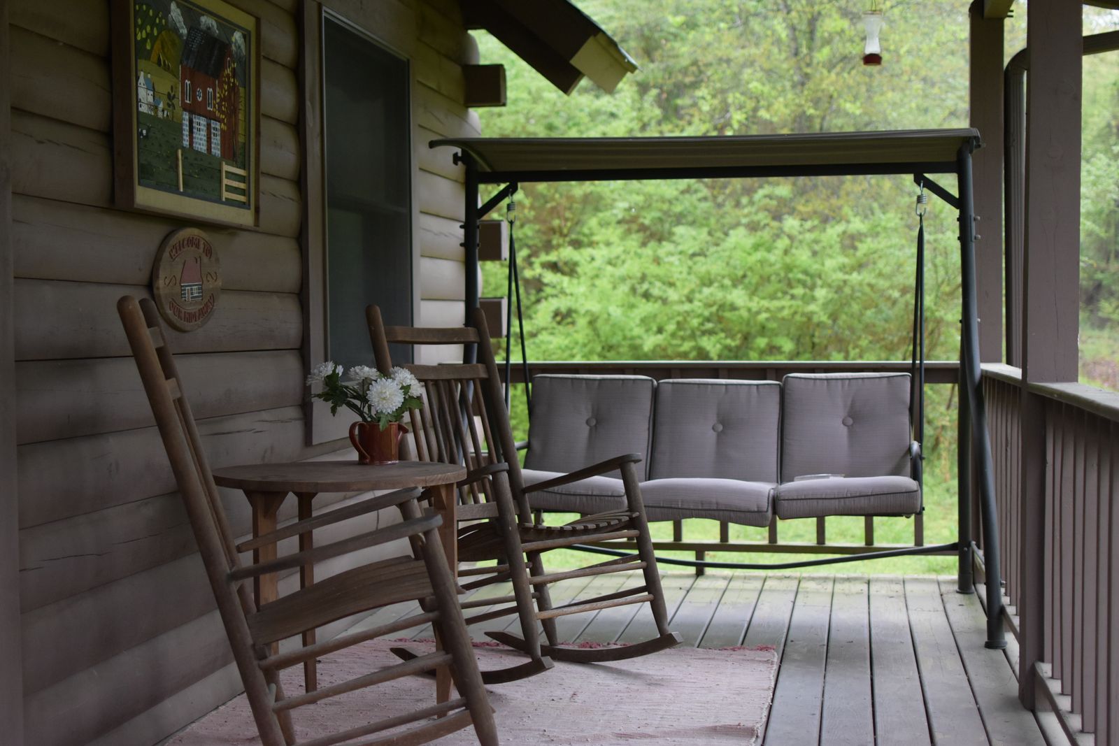 Cabin porch with rocking chairs and a swing among green trees